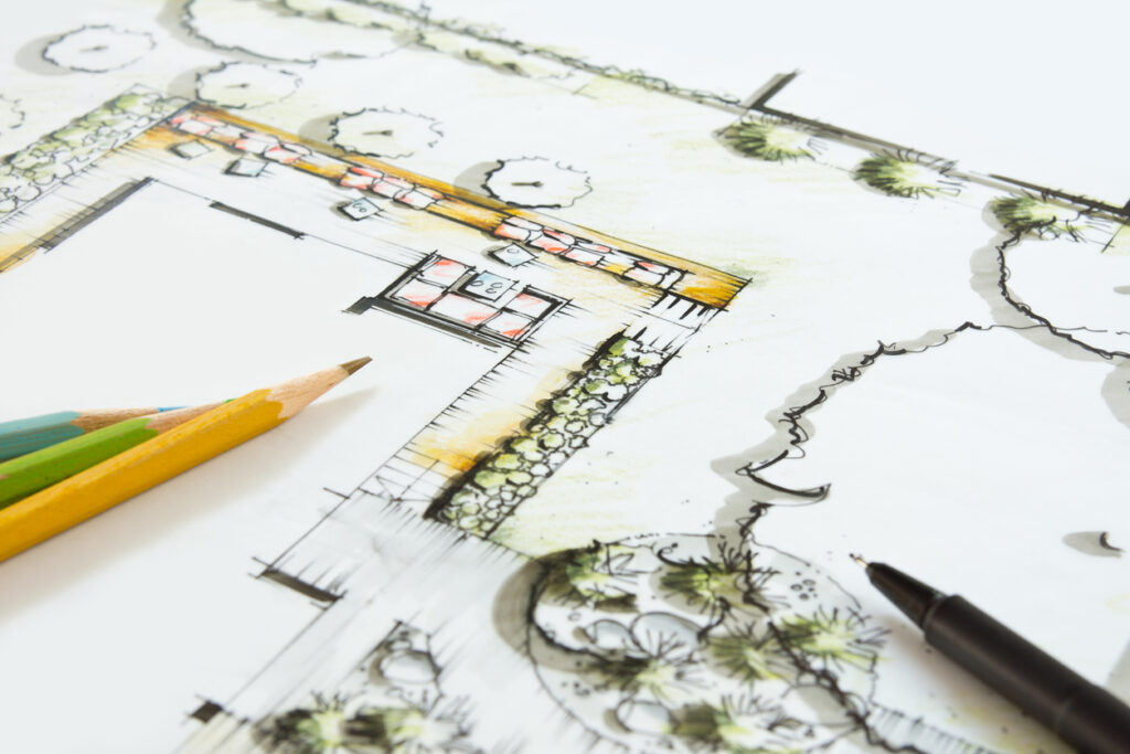 An architectural landscape sketch with vibrant color highlights lays beside a yellow pencil and a black pen on a white surface.