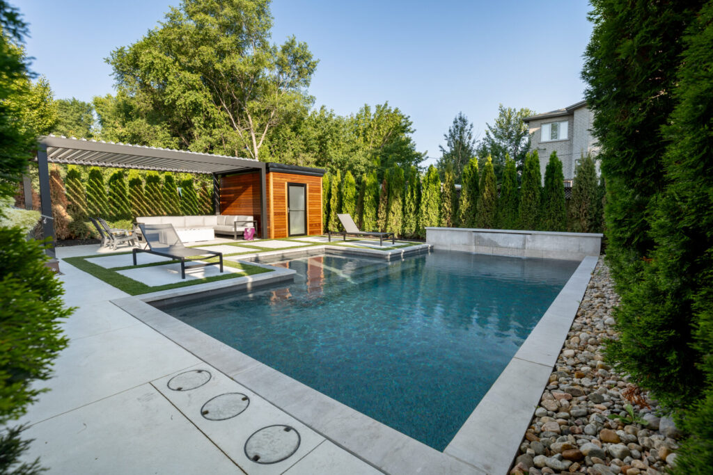A serene backyard with a modern swimming pool, surrounded by greenery, loungers, and a covered outdoor living space with comfortable seating.