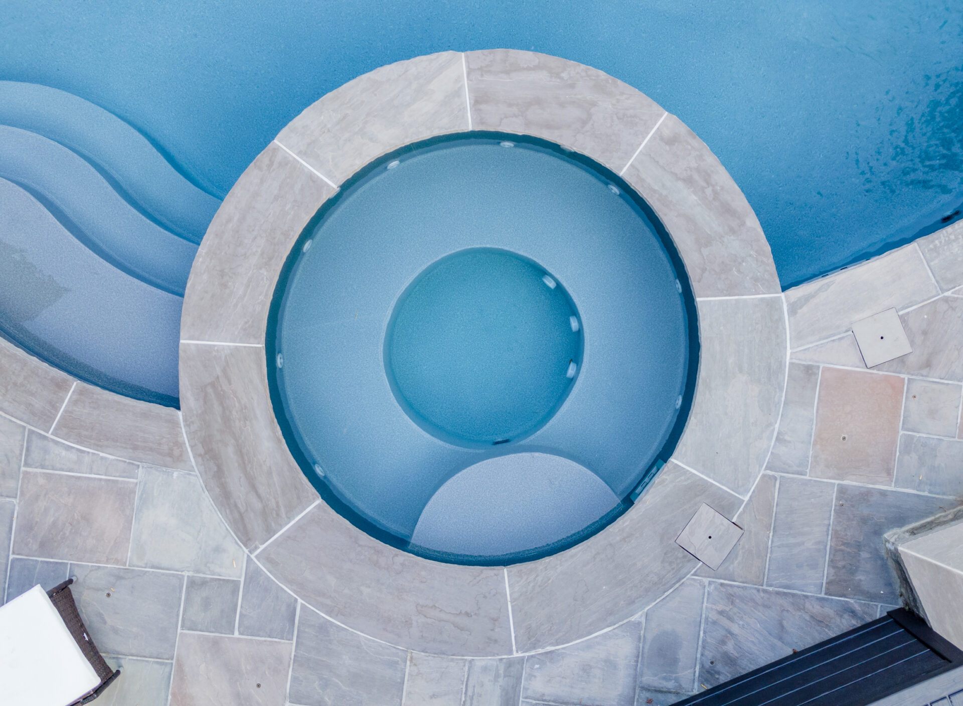 An aerial view shows a circular water feature with concentric rings, surrounded by a patterned tiled deck, giving off a serene, aquatic ambiance.