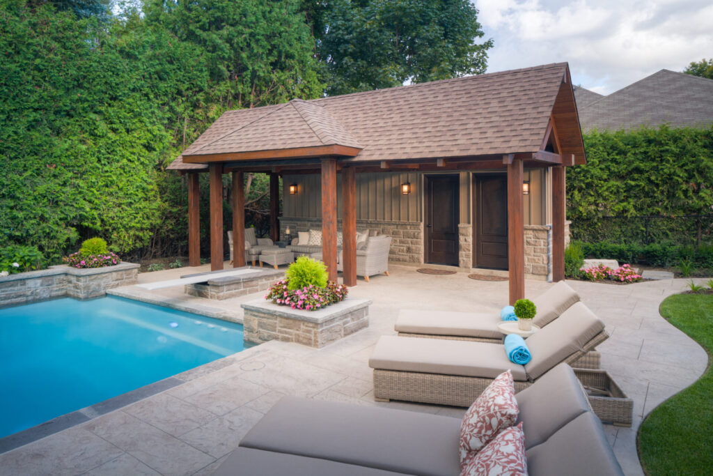 This image features a serene backyard with a swimming pool, a pavilion, comfortable outdoor furniture, lush greenery, and manicured landscaping under a clear sky.