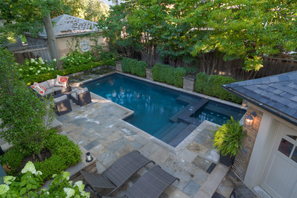 An elevated view of a serene backyard with a rectangular swimming pool, surrounded by plants, lounge chairs, and a cozy seating area.
