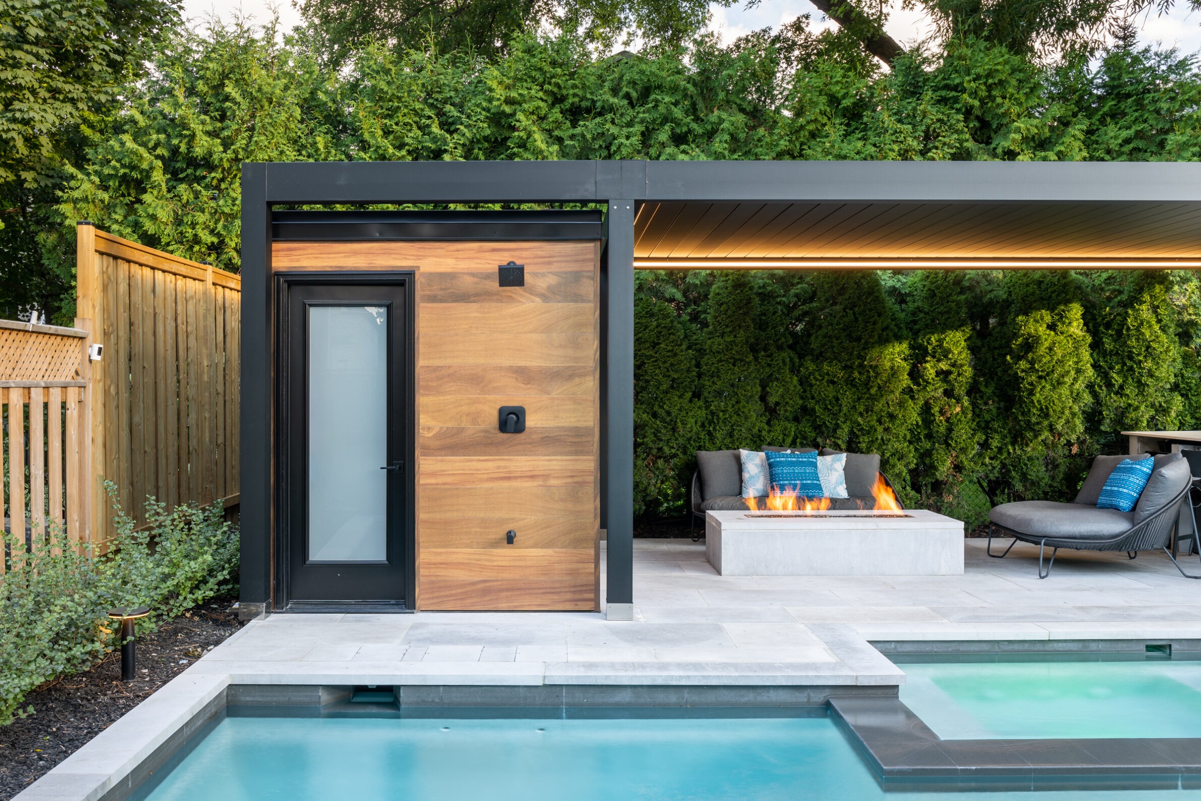 Modern backyard with a swimming pool, stylish wooden outbuilding door, outdoor fireplace, comfortable seating, and lush green privacy hedge.