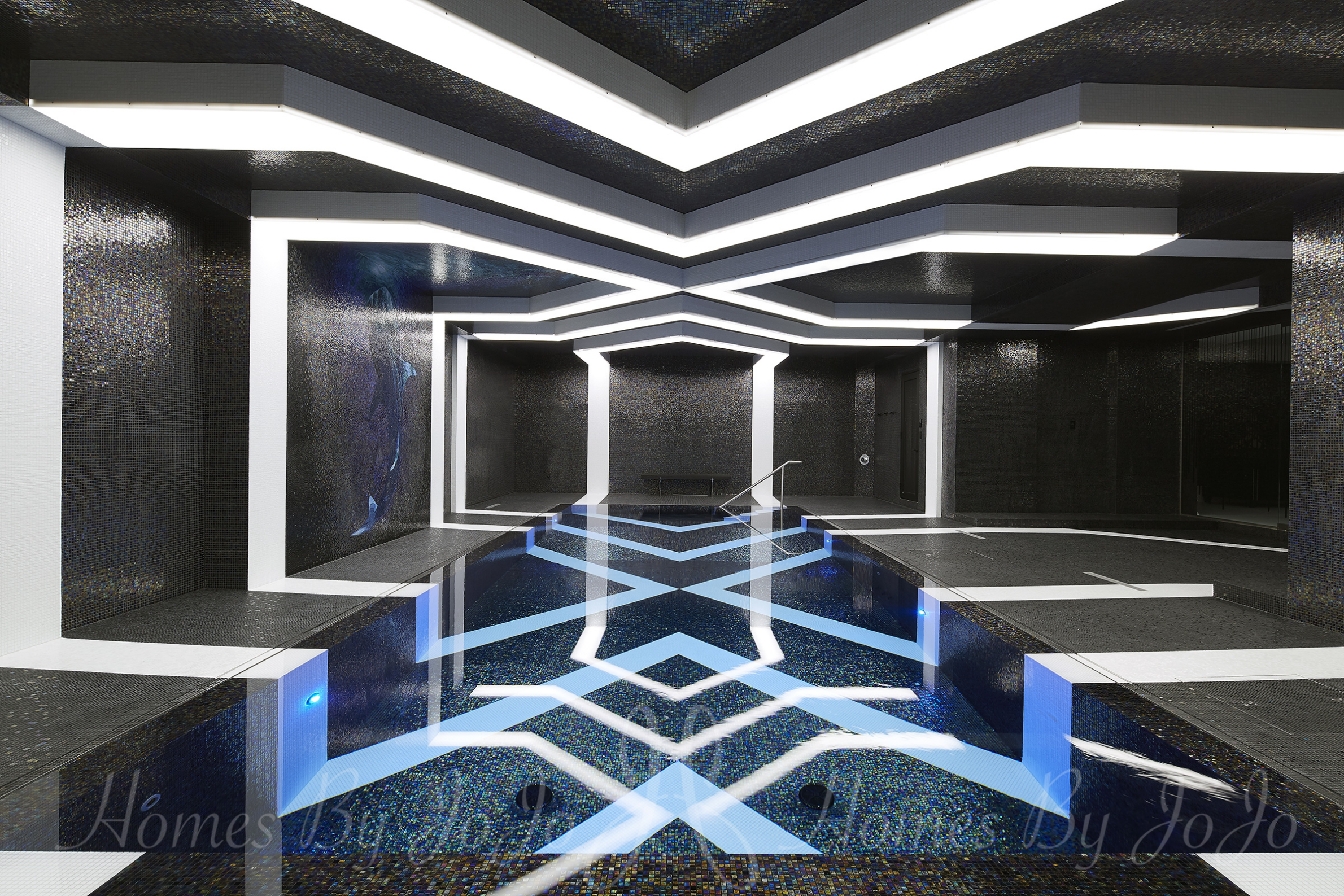 A futuristic indoor swimming pool with bold geometric patterns surrounded by raised white geometric lines on black walls