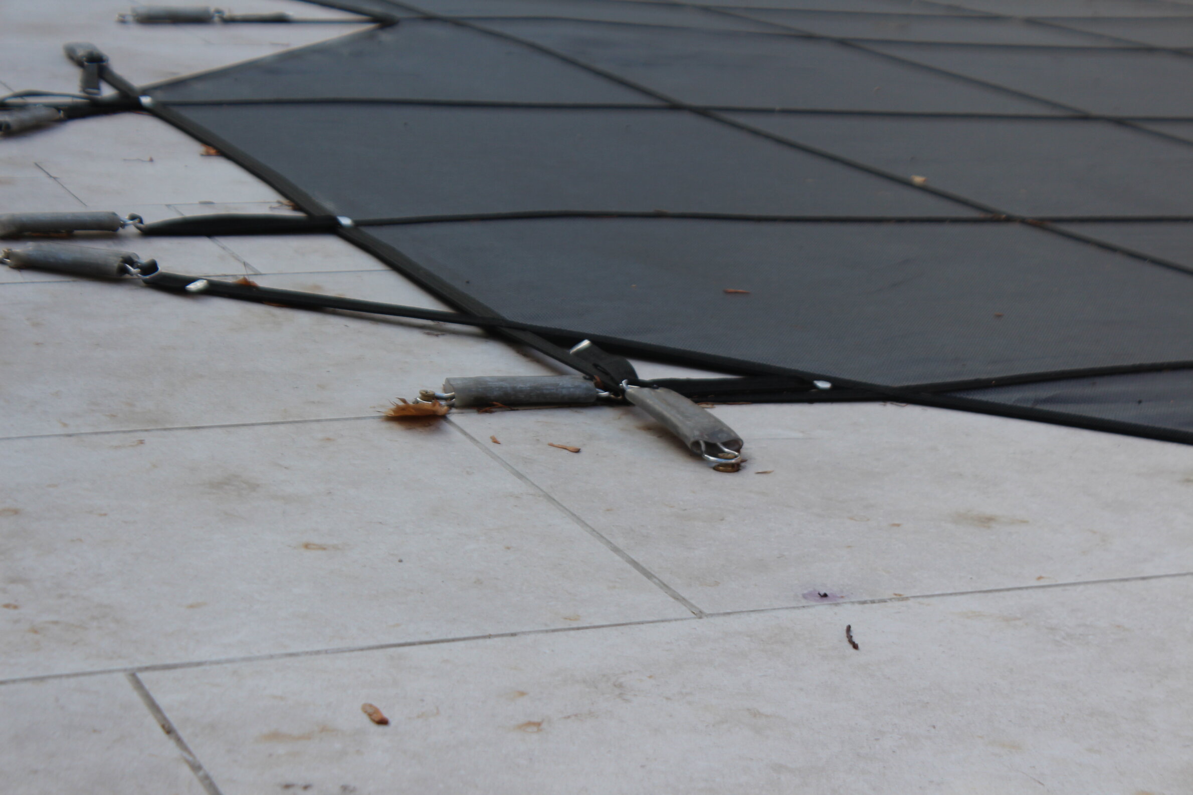 This image shows an outdoor flooring system with interlocking black panels, partially disassembled, revealing the underlying stone tiles and metal connectors.