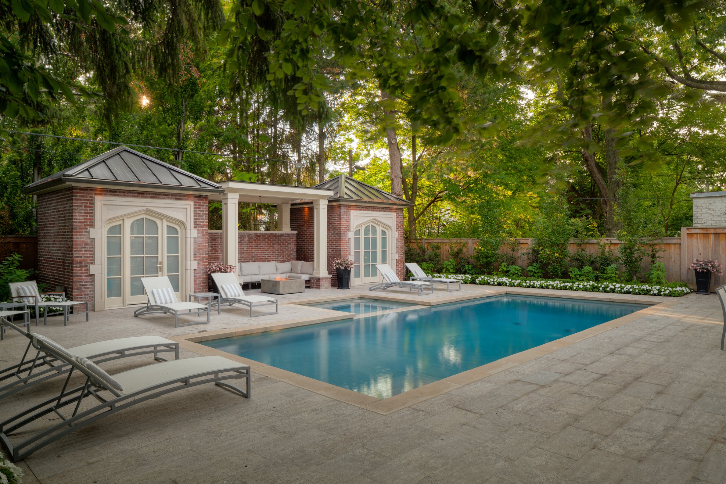 This image features an outdoor pool with loungers, surrounded by a lush garden, and adjacent to a building with a lounging area under a pergola.